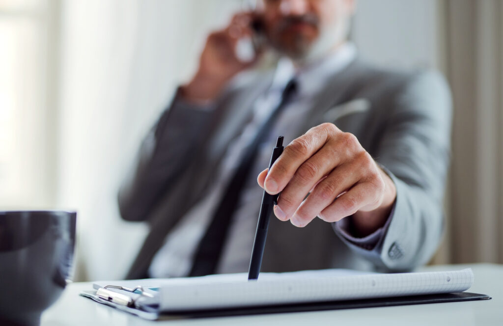 A midsection of businessman with smartphone sitting at the table, making a phone call.